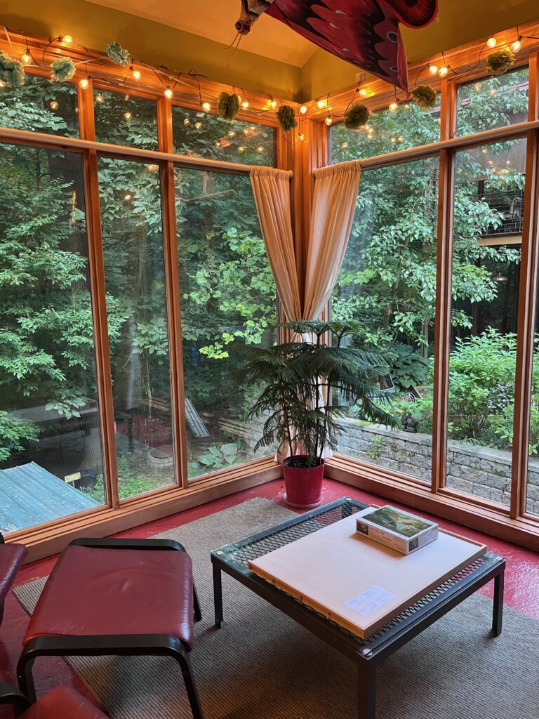 Windows looking out onto a forest with lights overhead, a short table and stool in front.