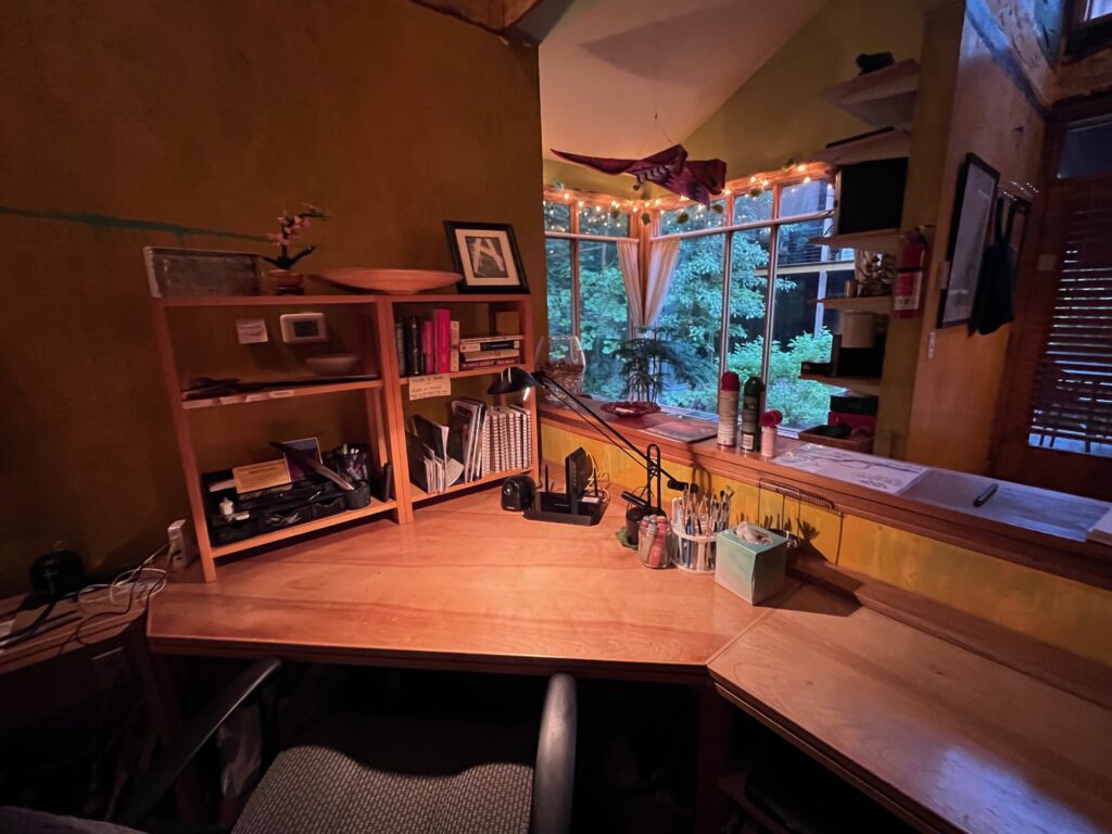 A desk in the foreground, with windows looking out onto a forest in the background.